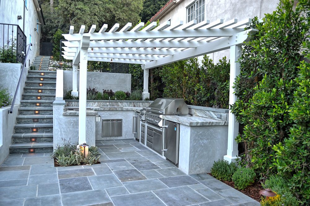 A white pergola with an outdoor kitchen in the middle of it.
