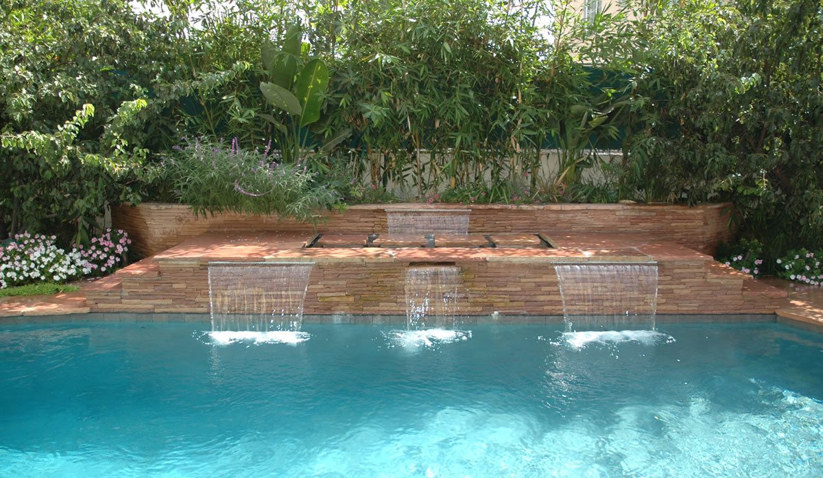 A pool with water falling into it and trees in the background.