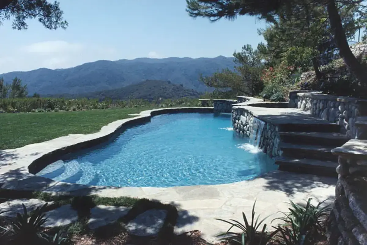 A pool with water falling into it and mountains in the background.
