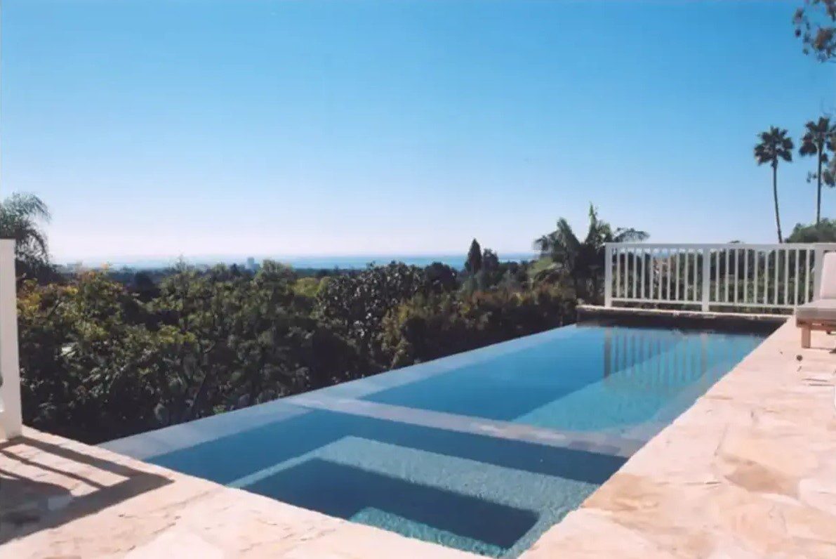 A pool with a view of the ocean and trees.