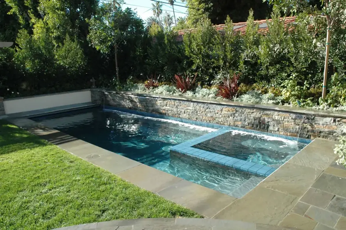 A pool with a stone wall and grass around it.