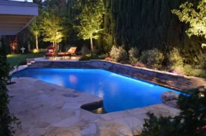 A pool with lights on and trees in the background